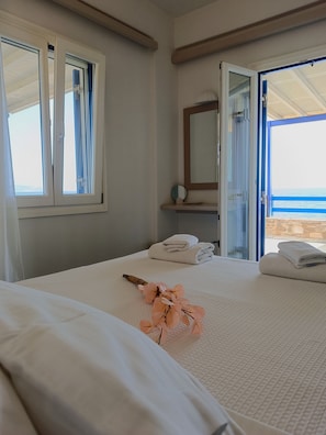 A bedroom with a bed, a window with curtains, a mirror, and a view of the sea.