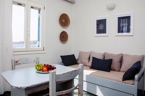 A room with a white table, a beige sofa, a window with a view, and two wall-mounted decorative plates.