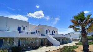 A white building with a stone base, a staircase, and a palm tree.