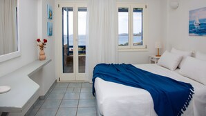 A bedroom with a bed, a nightstand, a lamp, a window with a view, and a door leading to an outdoor area.
