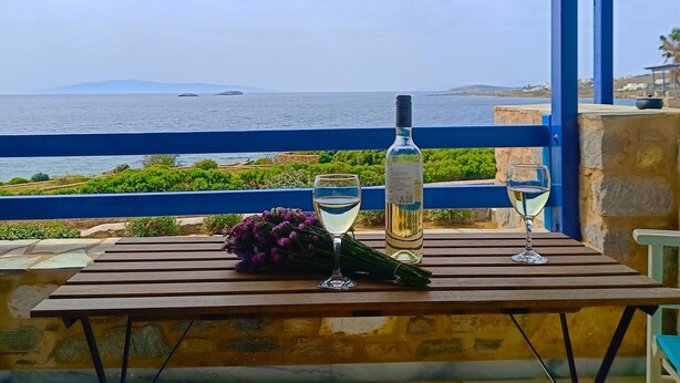Ein Tisch mit einer Flasche und einem Glas auf einem Balkon mit Blick auf das Meer.