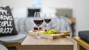 A room with a wooden table, a glass of red wine, a tray with grapes and cheese, and a pillow with text. - Semi-basement 'Deluxe Suite' Room with Wi-Fi and Air Conditioning (Naxos)