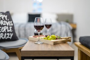 Een kamer met een houten tafel, een glas rode wijn, een dienblad met druiven en kaas, en een kussen met tekst.