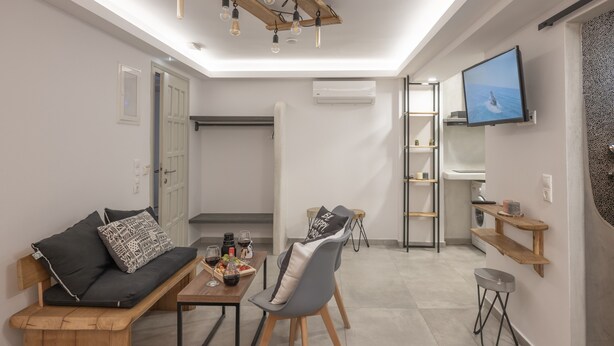 A modern living room with a sofa, a dining table, a TV mounted on the wall, and a wooden ceiling. - Semi-basement 'Deluxe Suite' Room with Wi-Fi and Air Conditioning (Naxos)