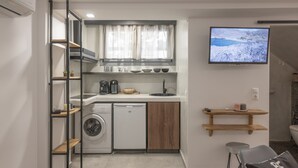 A compact kitchen with a washing machine, a coffee maker, and a TV mounted on the wall. - Semi-basement 'Deluxe Suite' Room with Wi-Fi and Air Conditioning (Naxos)