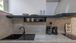 Une cuisine compacte avec un évier noir, une machine à café et une étagère où sont rangées des tasses et des bols.