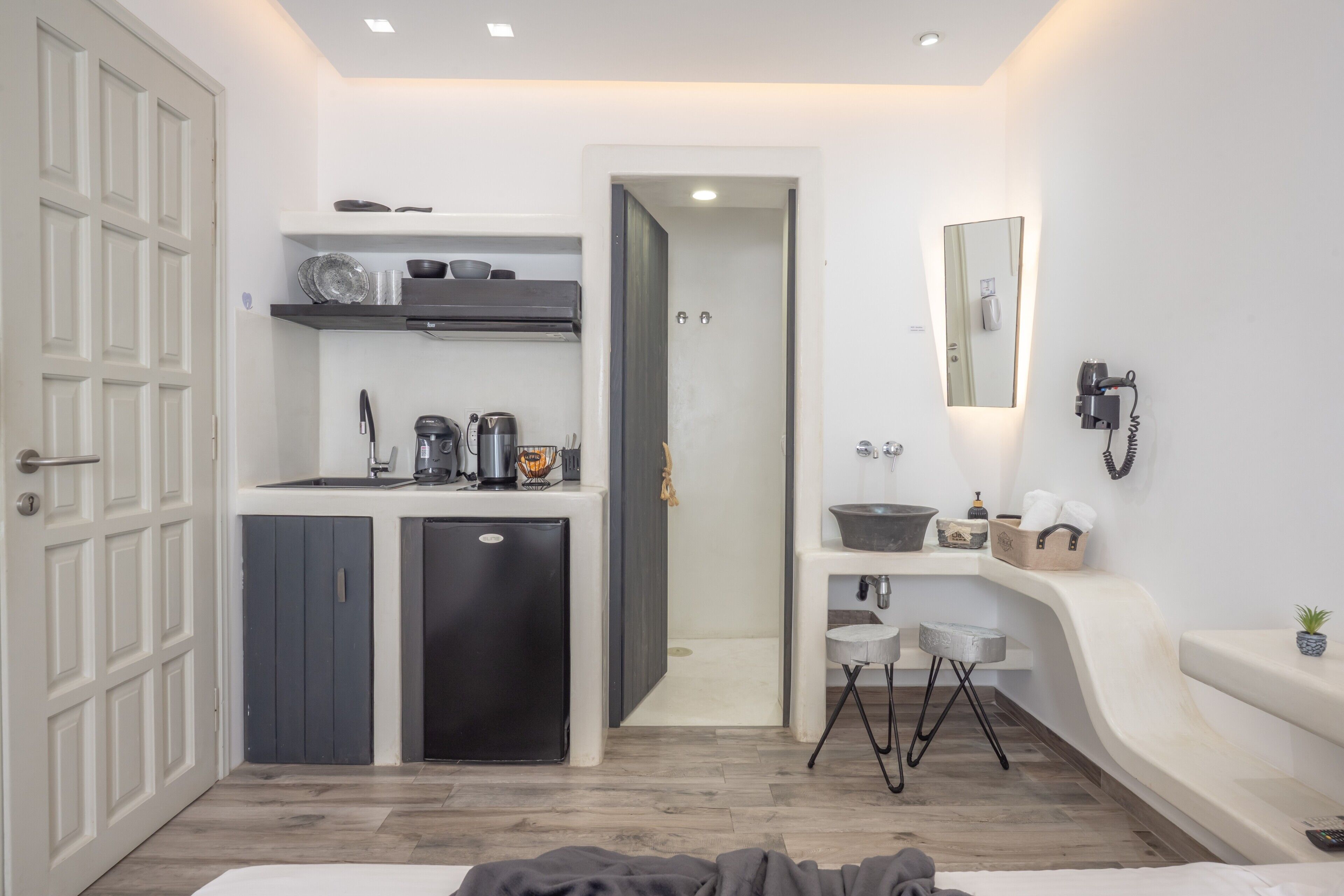 Een kleine hotelkamer met een kitchenette, een badkamer met spiegel en wastafel, en een bed.