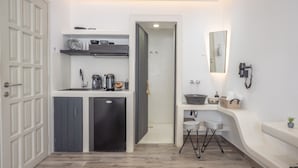 Una habitación de hotel pequeña con kitchenette, un baño con espejo y lavamanos, y una cama.