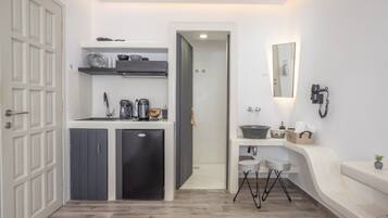 Een kleine hotelkamer met een kitchenette, een badkamer met spiegel en wastafel, en een bed.