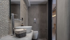 Un bagno con parete in pietra, un lavandino bianco, un water bianco e un cesto sul ripiano.