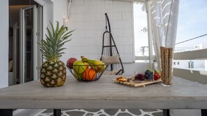 Et bord med en ananas, en frugtkurv, snacks og et glas juice på en balkon.