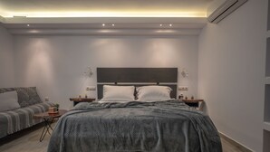 Ein modernes Schlafzimmer mit einem großen Bett, Nachttischen, einem Sofa und einem kleinen Tisch mit einer Pflanze.