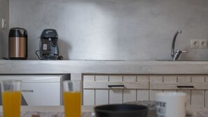 Eine Küche mit Kaffeemaschine, Wasserkocher und Spüle. Auf der Arbeitsfläche stehen Gläser Orangensaft und eine Schüssel.