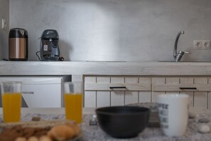 A kitchen with a coffee maker, kettle, and sink. There are glasses of orange juice and a bowl on the counter.