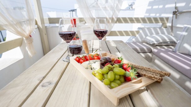 Une table en bois avec une planche à fromage, des raisins, des fraises et des verres à vin.