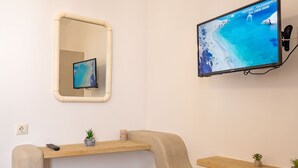 Une salle de bain avec un miroir, une télévision et une étagère en bois sur laquelle est posée une plante.