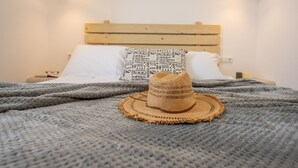 Un lit avec une tête de lit en bois, un coussin à motifs, un chapeau de paille et une couverture tricotée grise.
