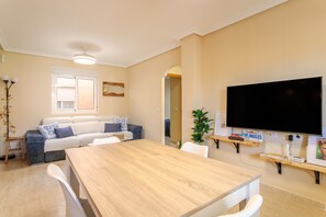 Un salon moderne avec un canapé, une table à manger et un téléviseur à écran plat fixé au mur.