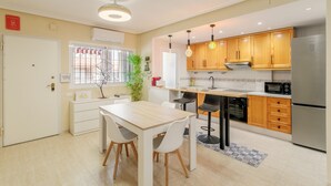 Cuina moderna amb armaris de fusta, un frigorífic d'acer inoxidable i zona de menjador amb taula i cadires.