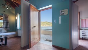 A room with a wooden door leading to a balcony, a small table, a bench, and a wall clock. - Apartment 'Kymothoi' with Sea View, Wi-Fi and Air Conditioning (Ithaca)