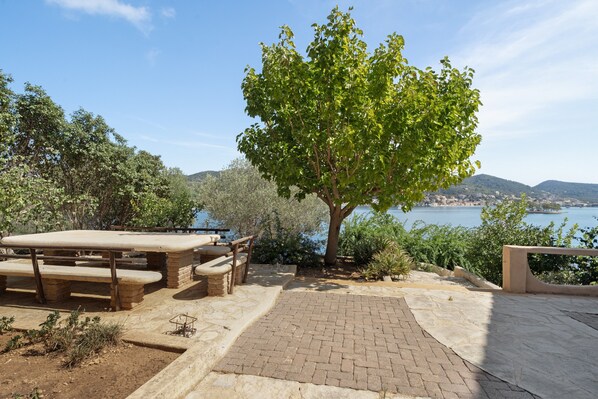 A picnic table and benches near a tree overlooking a body of water.