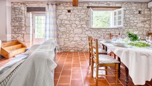 Une salle à manger rustique avec un mur en pierre, des poutres en bois, une longue table dressée pour quatre personnes et un banc le long du mur.