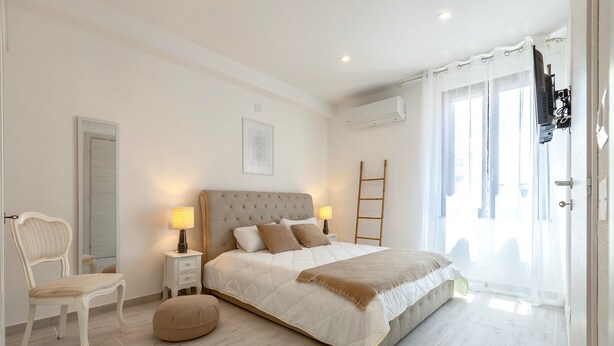 A bedroom with a bed, bedside tables, a chair, a ladder, and a window with curtains. - Apartment 'Attico 29 Alghero' with Balcony, Wi-Fi and Air Conditioning (Alghero)