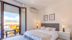A bedroom with a bed, bedside lamps, a nightstand, a window with blinds, and a balcony with a table and chairs. - Apartment 'Attico 29 Alghero' with Balcony, Wi-Fi and Air Conditioning (Alghero)