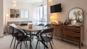 A modern living room with a dining table, chairs, a sofa, a TV, a mirror, and a cabinet with decorative items. - Apartment 'Attico 29 Alghero' with Balcony, Wi-Fi and Air Conditioning (Alghero)