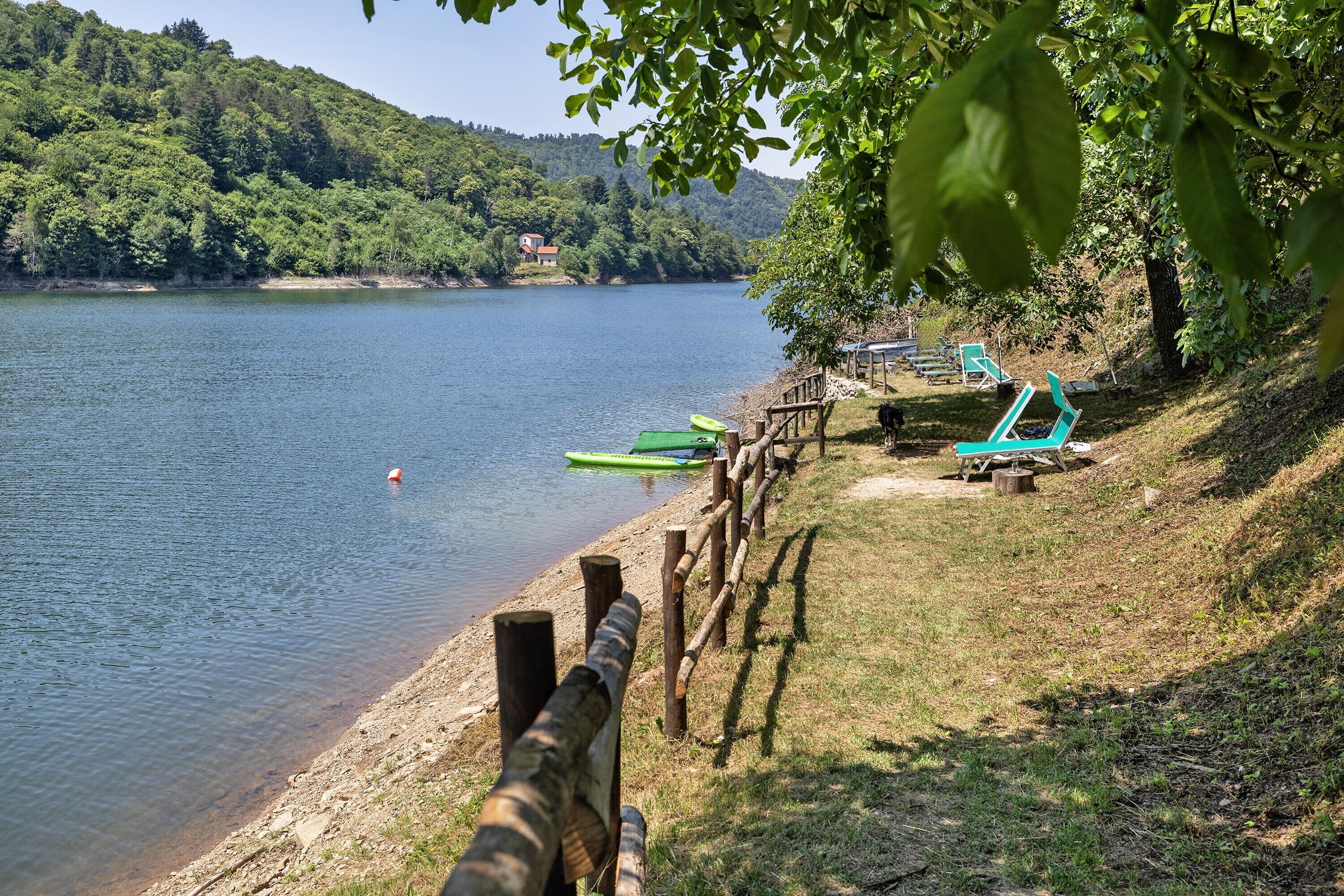 Une vue sur le lac, avec une clôture en bois, une rangée de chaises vertes et un petit bâtiment en arrière-plan.