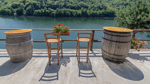 Una terraza con dos barriles de madera, una mesa con sillas y una maceta.