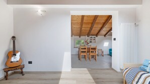 Una habitación con una guitarra de madera, una cama con ropa de cama a rayas y una zona de comedor con sillas y una mesa.