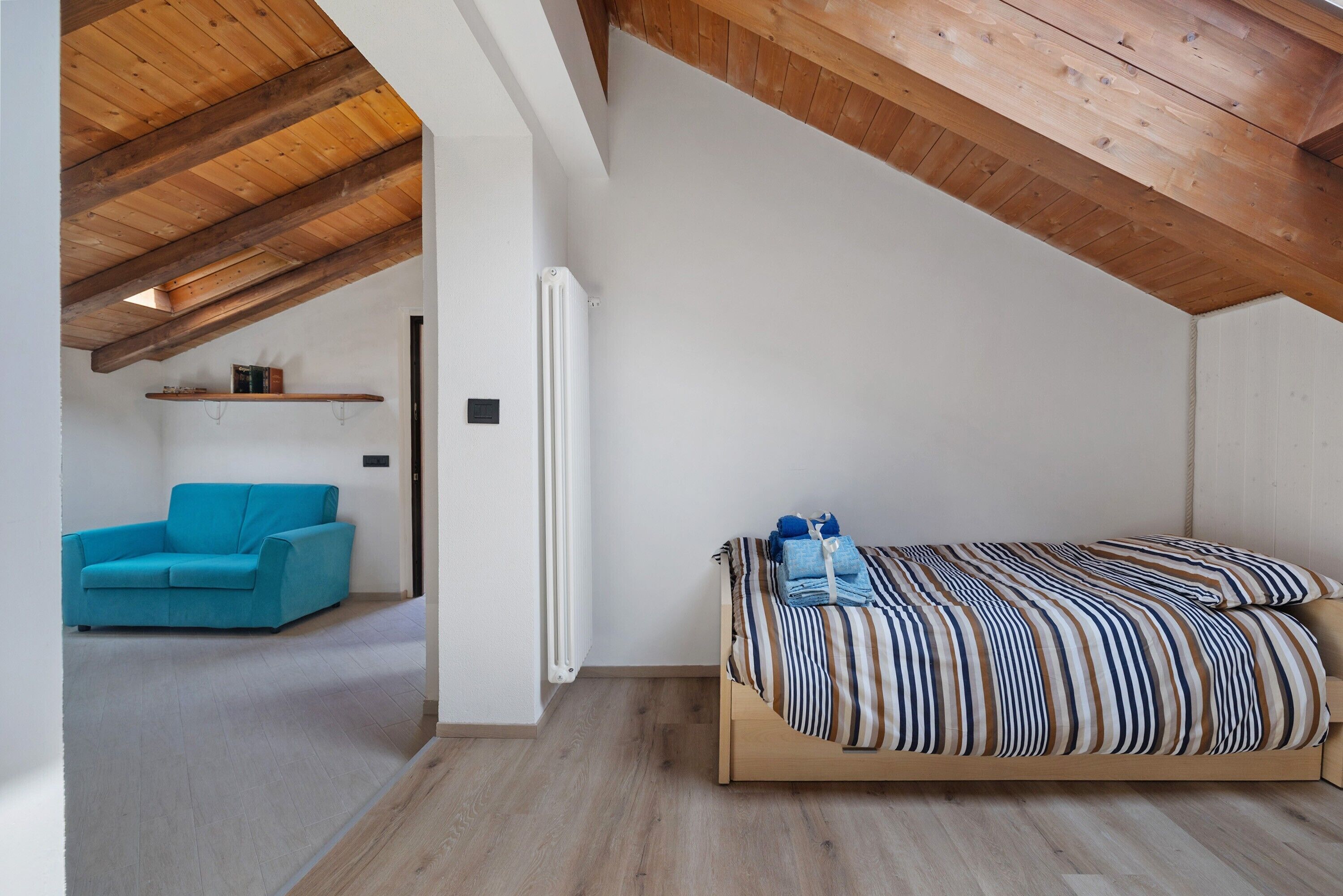 Un dormitorio con techo inclinado, cama con ropa de cama a rayas, sofá azul y un radiador.