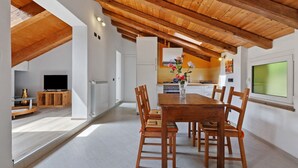 Un comedor con mesa y sillas de madera, una cocina al fondo y un ventanal grande.
