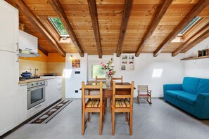 Une cuisine avec des poutres en bois, une table à manger avec des chaises, un canapé et une fenêtre donnant sur un beau paysage.
