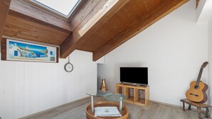 Una habitación con techo de madera, un cuadro, un reloj, un televisor, una guitarra y una mesa redonda de madera con cubierta de vidrio.