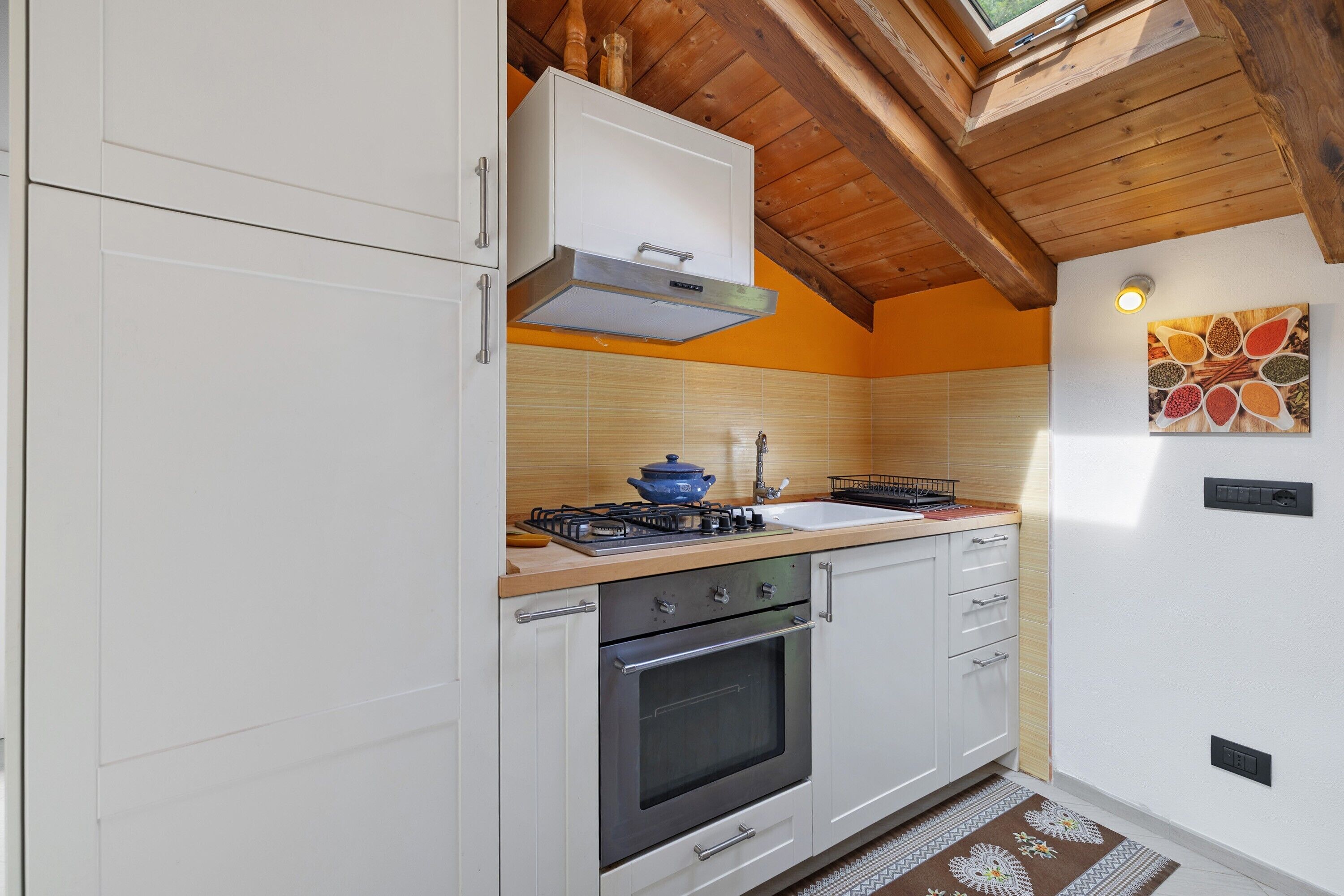 Eine Küche mit weißen Schränken, einem Gasherd, einem Backofen, Holzbalken an der Decke und einer Wandleuchte.