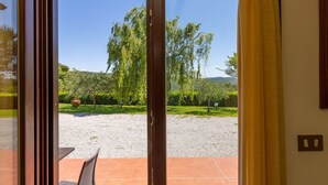 Blick durch eine Glastür auf eine Terrasse mit Kiesweg, Pflanzen und Bäumen.