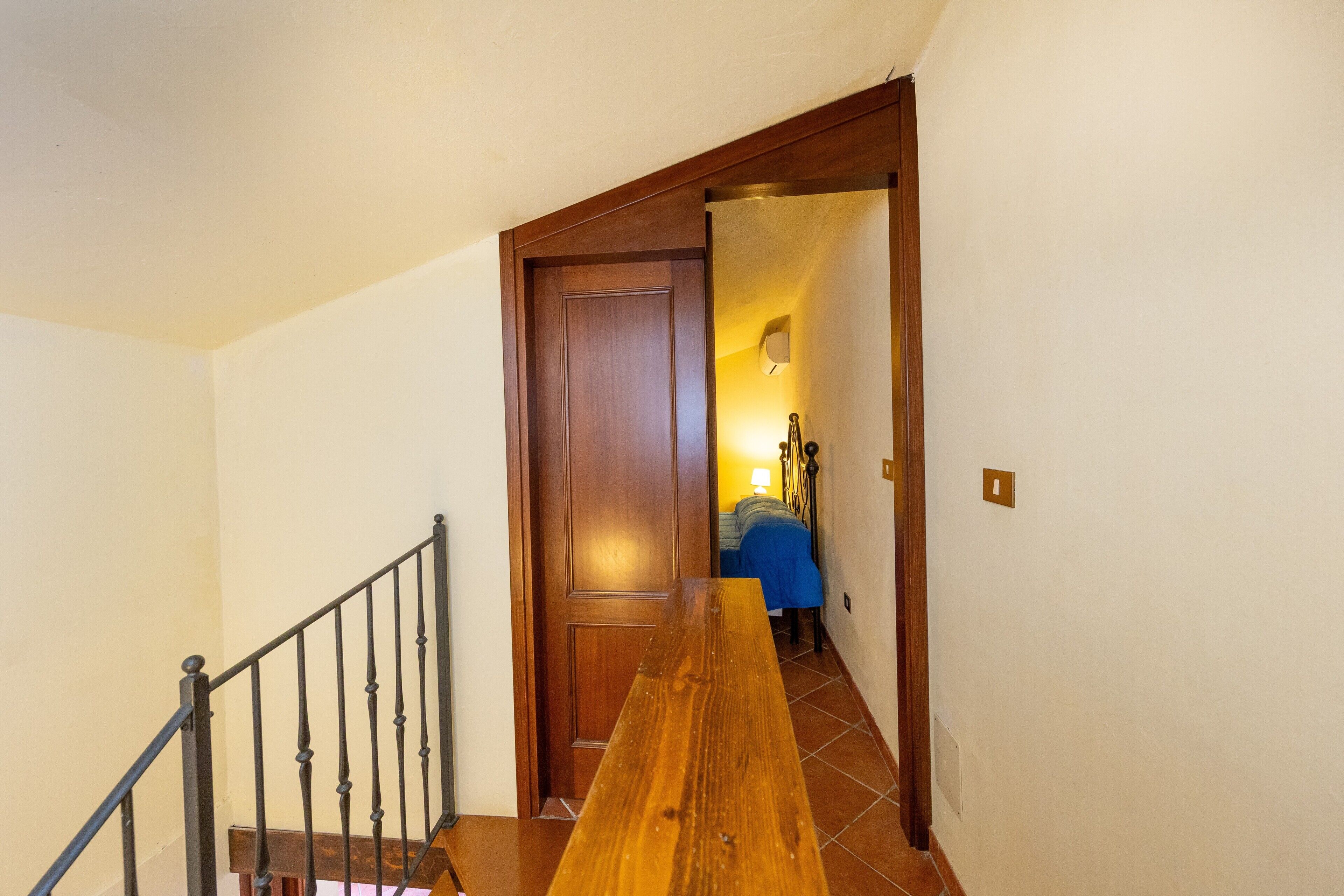 A wooden staircase with a metal railing leading to a room with a bed and a lamp.