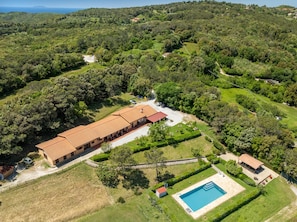 An aerial view of a property with a large building, a swimming pool, and surrounding greenery.