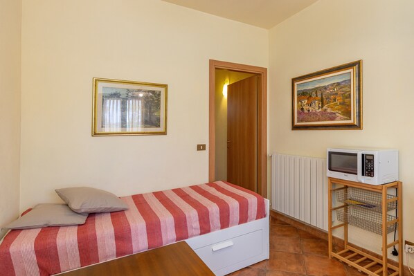 Una habitación pequeña con una cama, un microondas sobre un mueble, una puerta y dos cuadros en las paredes.