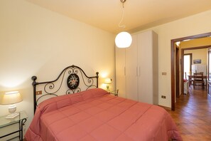 Ein Schlafzimmer mit einem Bett, Nachttischlampen, einer Wanduhr und einer Tür zu einem anderen Raum.