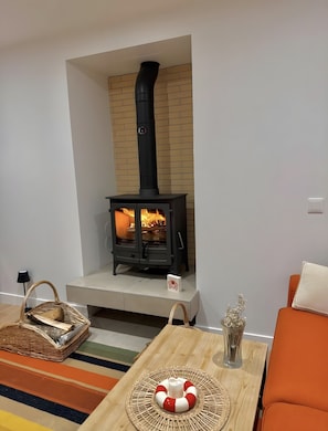 A modern living room with a wood-burning stove, a wicker basket, a striped rug, and a cushioned chair.
