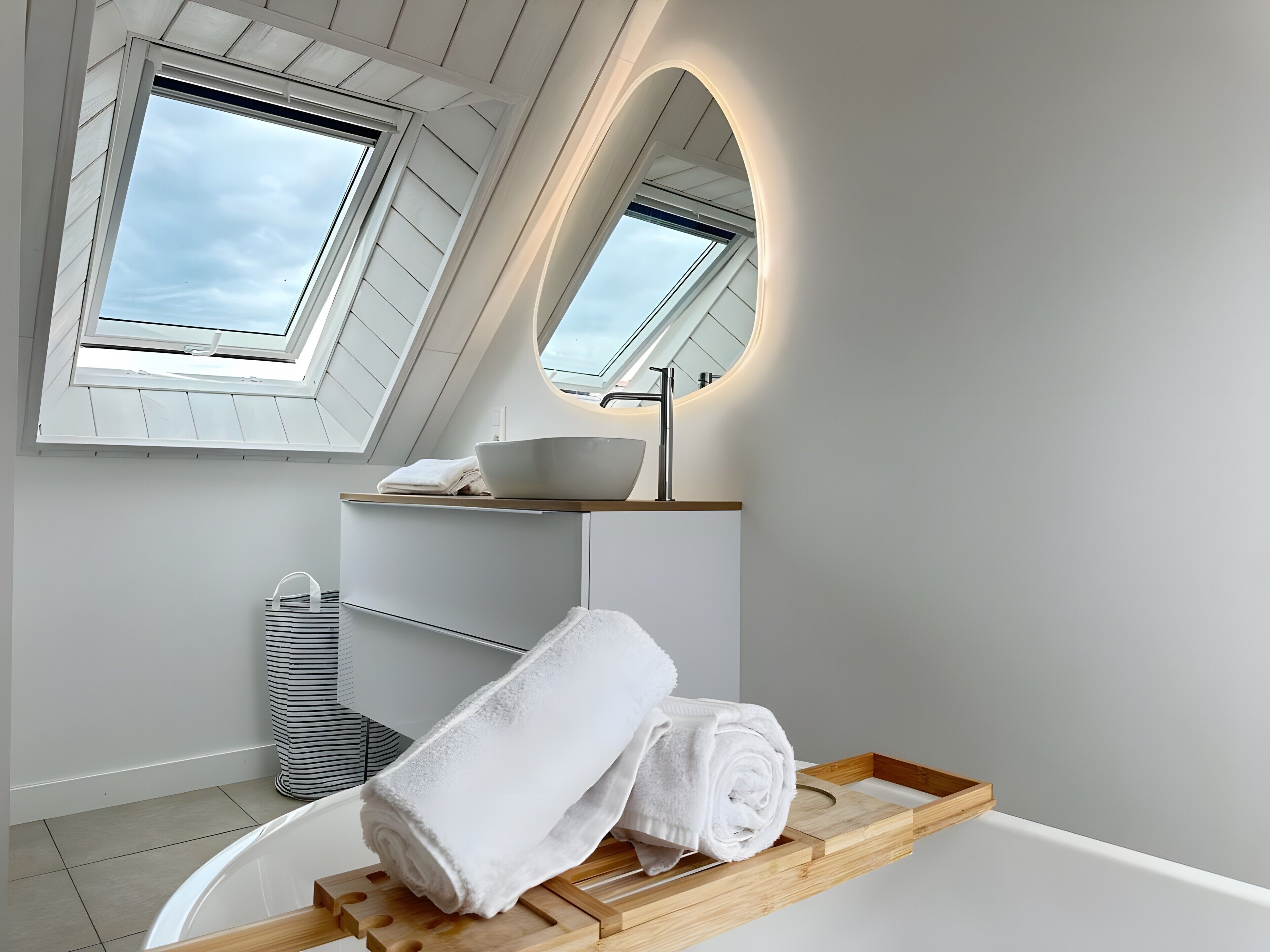Ein modernes Badezimmer mit Oberlichtern, einem großen Spiegel, einem Holzwaschtisch und einer Badewanne.