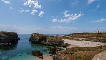 A coastal landscape with rocky formations, clear water, and a lighthouse.