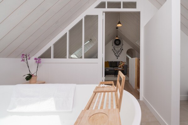 A modern bedroom with a sloped ceiling, a wooden bed frame, a white wall, and a hanging dreamcatcher.