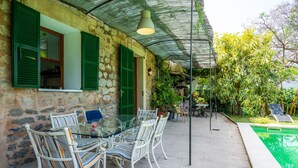 Ein Steinhaus mit einem Glastisch, Stühlen, einem Pool und einer überdachten Terrasse.