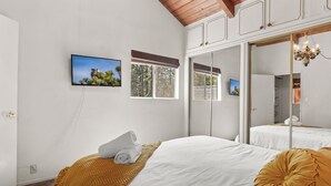 A bedroom with a bed, a large mirror, a television, and a window with blinds.