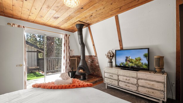 A bedroom with a large bed, a fireplace, a television, and a dresser.