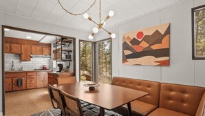A modern kitchen with wooden cabinets, a dining area with a brown leather booth, and a large window offering a view of trees.
